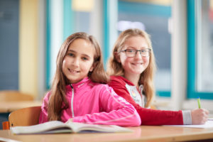 Zwei Schülerinnen lächelnd am Schreibtisch