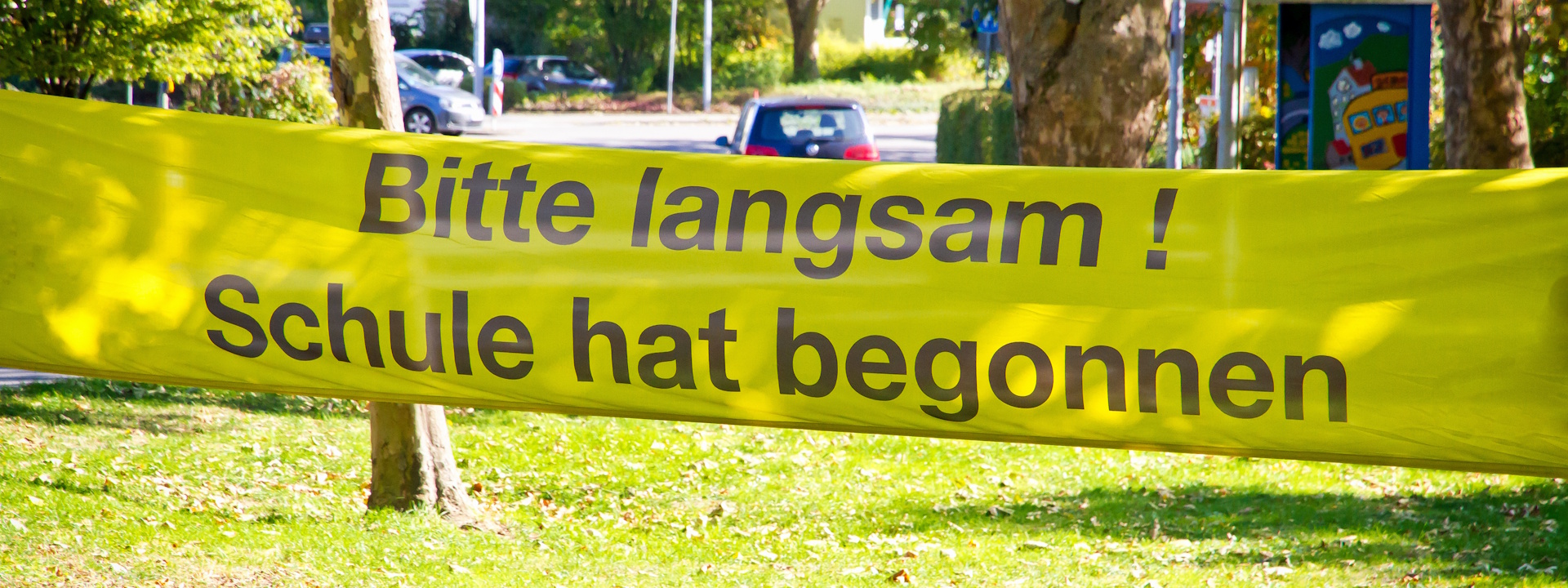 Ein Banner an einer Straße mit Aufschrift: Bitte langsam, Schule hat begonnen